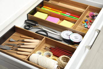 Fototapeta na wymiar Sewing accessories and stationery in open desk drawer indoors