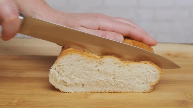 Woman cuts bread with knife on wooden board closeup.