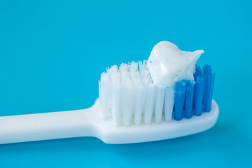 Closeup blue and white tooth brush with toothpaste, blue background, selective focus