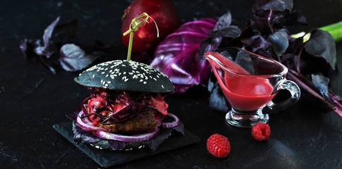 Black burger with berry sauce on a dark background. Inside the cutlet, red onions, purple basil, red cabbage and berry home-made vinaigrette. trendy burger with violet content. copy space
