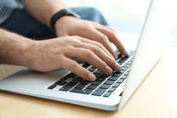 Man working on modern laptop at wooden table indoors, closeup