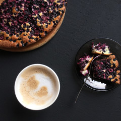 Delicious homemade berry pie and cup of coffee cappuccino on dark black stone background. Top view of blueberry, bilberry tart with cup of coffee latte with milk froth. Square image