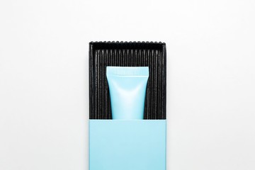Close-up of cosmetic cyan tube with mock-up, packaging in black and blue box on white background.
