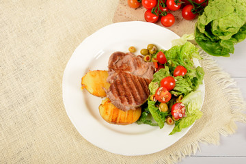 two pieces of grilled potato and grilled meat next to lettuce with tomatoes and olives on a white plate