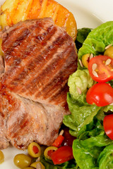 two pieces of grilled potato and grilled meat next to lettuce with tomatoes and olives on a white plate