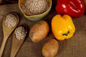 barley in a bowl next to raw peppers, dried mushrooms, potatoes and dried spices