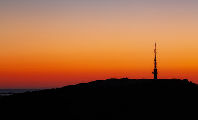 Silhouette Tv radio-tower during sunset. Warm orange sky.