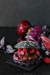 Fashion black burger with raspberries and  berry sauce. On a dark background. Inside the cutlet, red onions, purple basil, red cabbage and raspberry homemade vinaigrette. 