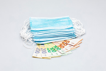 stack of banknotes fan-shaped under a stack of blue surgical masks isolated on a white background