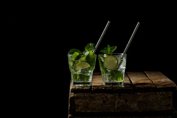 Mojito cocktail with lime, ice cubes and mint in a glass on a black rustic table. Mojito on a background of gray stone.
