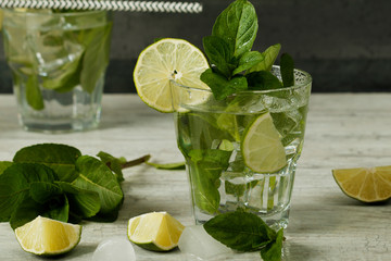 Mojito cocktail with lime, ice cubes and mint in a glass on a black rustic table. Mojito on a background of gray stone.