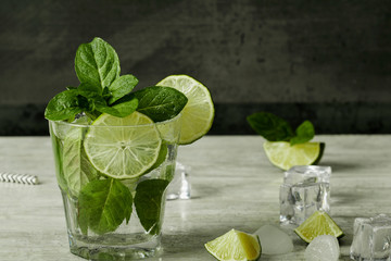 Mojito cocktail with lime, ice cubes and mint in a glass on a black rustic table. Mojito on a background of gray stone.