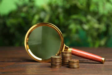 Coins and magnifying glass on wooden table against blurred background. Search concept