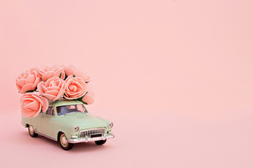 Green retro toy car delivering a bouquet of flowers on a pink background. Postcard February 14, Valentine's Day. Flower delivery. March 8, International Happy Women's Day.