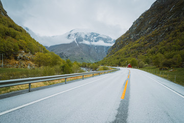Fototapeta premium Asfaltowa droga prowadząca między wysokimi ośnieżonymi górami