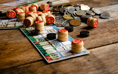 Boardgame of "lotto", wooden barrels with numbers cards chips and coins on a wooden table.