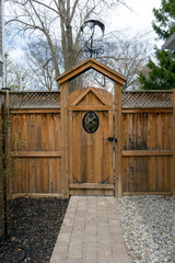 A cedar fence with iron inset, a tumbled paver walkway, mulch and pea gravel make a low maintenance entrance into the garden.