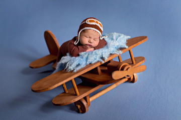 Portrait of a 5 day old newborn baby boy in a suit and cap. Aviator with glasses. He sleeps, posing on an old wooden airplane.