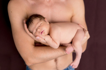 Newborn 5 day naked boy, lies in his father's arms and sleeps. Happy young dad with a naked torso holds a newborn son in his arms.