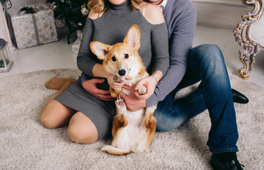 couple expecting a baby sitting on the floor and holding a corgi