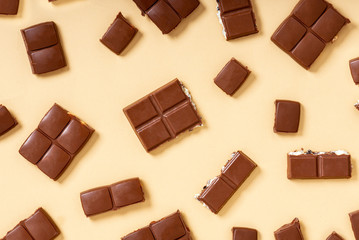 Pieces of milk chocolate on a beige background top view. Chocolate background, sweet food.