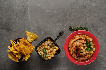 Flat lay Hummus with sun dried tomatoes in clay dish topped with chickpeas and green coriander leaves on stone table served with tortilla chips