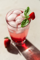 A glass of strawberry basil lemonade with ice and sunny shadow. Vertical.