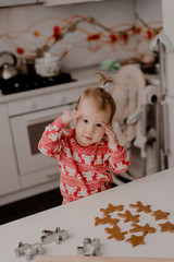 Little girl 2 years old sitting in the kitchen in red pajamas, messing with flour, baking...