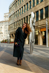 Fashion outdoor photo of happy young woman with red hair in elegant clothes and luxurious coat, walking by the city.