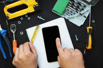male hands with a measuring tape and pen write in a notebook in a box and tools for repair and...