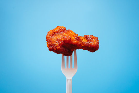 Korean style fried chicken on plastic fork with blue background, fast food Concept. 