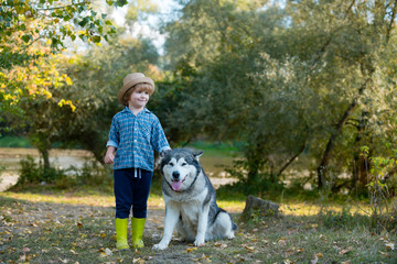 Naklejka na ściany i meble Funny children boy with dog walk together on green field. Adventure and vacations children concept. Children are hiking together with pet dog. Kids with cute dog.