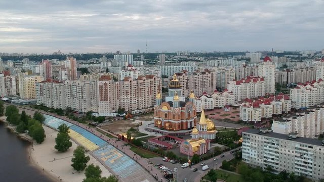 Aerial photography. Orthodox Christian Church on the Obolonskaya embankment in the spring in Kiev. Many houses built along the Dnieper Bay. Drone.