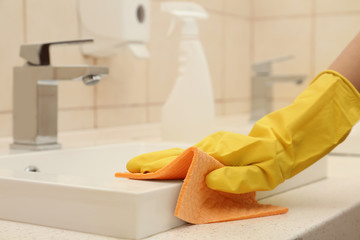 Woman cleaning sink with rag in bathroom, closeup