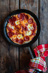Sourdough breakfast pan pizza with pepperoni in a skillet on wooden surface