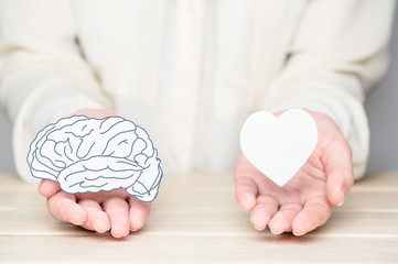 Female hands holding paper cut brain and soul. Conflict between emotions and rational thinking....