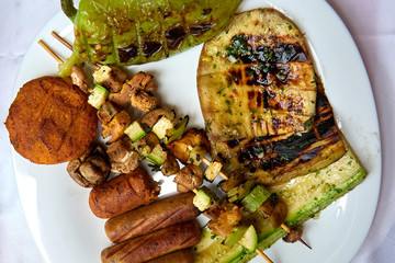 Vegan barbecue on a white plate with vegetables and vegan sausages  and hamburger