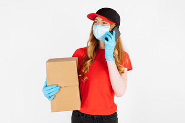 The courier, wearing medical rubber gloves and a mask, holds cardboard boxes and talks on the phone on a white background.