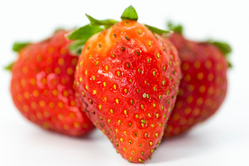 Three natural strawberries with leaves on white background.
