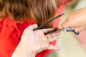 Close up of hairdresser hands cutting brown hair at home. Professional stylist trimming hair split ends.