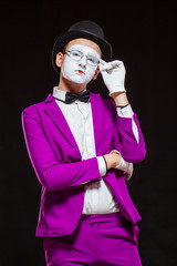Portrait of male mime artist, isolated on black background. Young man in purple suit is touching...