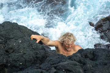 young man stands on a rock and is preparing to jump into the ocean