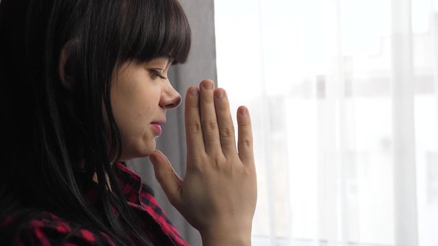 brunette girl makes a wish prayers bedtime religion concept. prayer woman mom indoors lifestyle praying by bed front of window