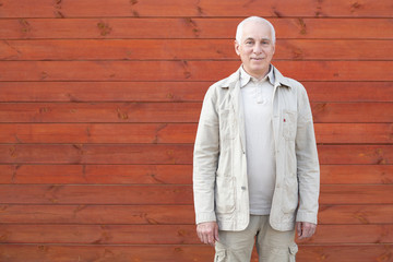 Elderly man smiling outdoors on wooden wall background, happy successful businessman.