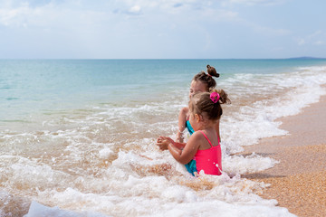 Two sister girls in swimsuits playing on the beach with toys and sand on a sunny summer day. Fun family vacation at the sea. Kids activity outdoors