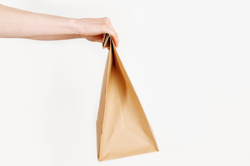 The courier holds a paper bag with food on an isolated white background. Fast and free delivery. Online stores