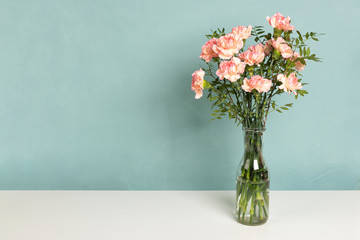 Vase with a beautiful pink carnation flowers on white table. Pastel green background, copy space for your text