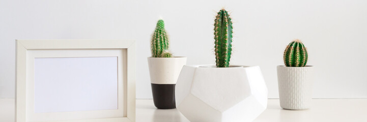 Desk on a white empty wall background with three cactuses in a geometric pot and a frame mockup. Copy space. Panorama