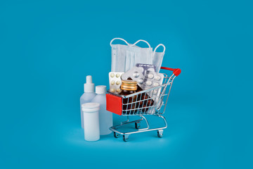 Medicine bottles with pills and medical masks in a shopping cart on a blue background.
