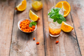 Sea buckthorn ice lemonade with oranges. Fruits and berries outdoors on a wooden table. Detox drinks.